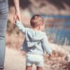 A baby is walking holding their mother's hand