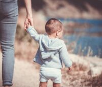 A baby is walking holding their mother's hand