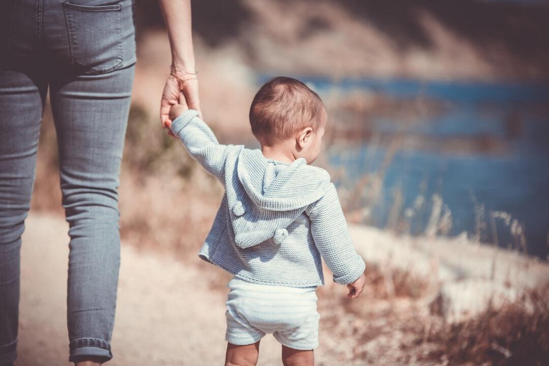 A baby is walking holding their mother's hand