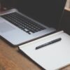 A notebook and pen are placed on the bench with a laptop