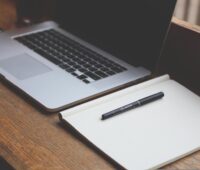 A notebook and pen are placed on the bench with a laptop