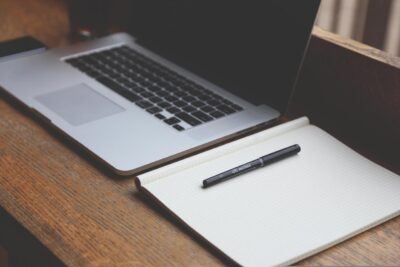 A notebook and pen are placed on the bench with a laptop