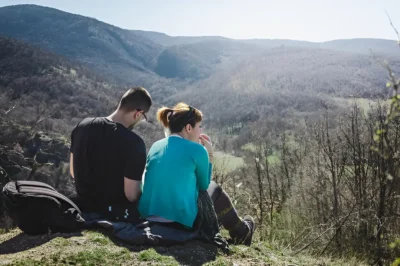 Couple sitting on mountain against clear sky