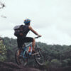 man with bicycle standing on mountain against sky