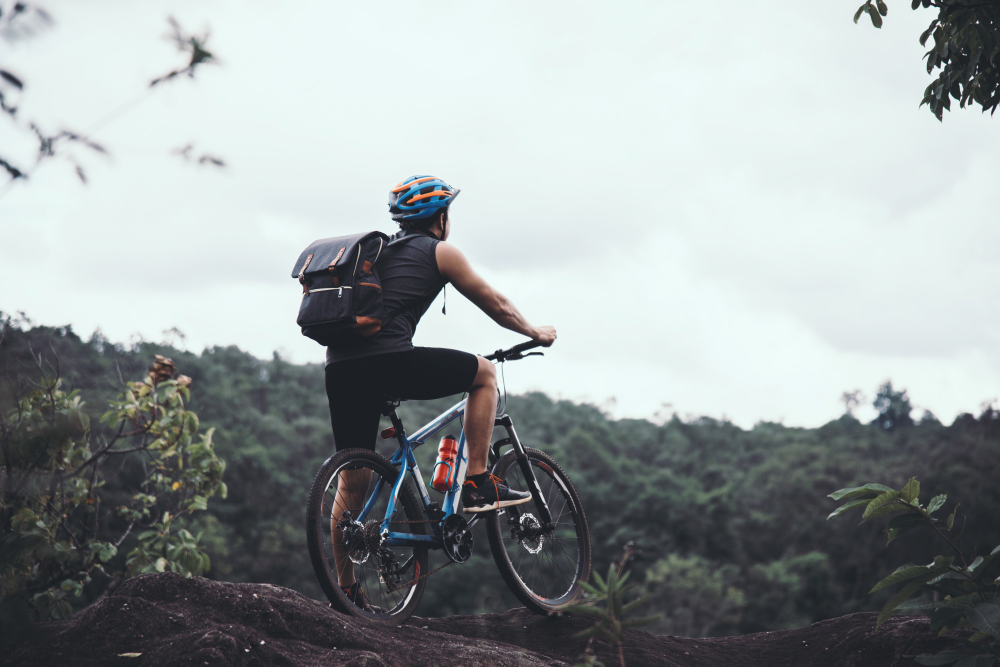 man with bicycle standing on mountain against sky