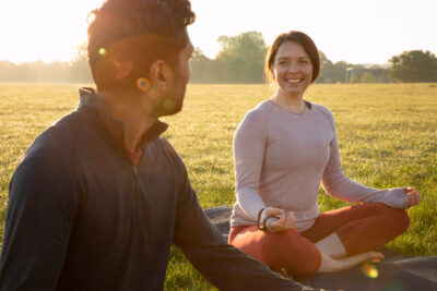 Smiley woman and man meditating outdoors on yoga mat
