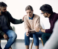 Young sad woman being consoled during group counselling
