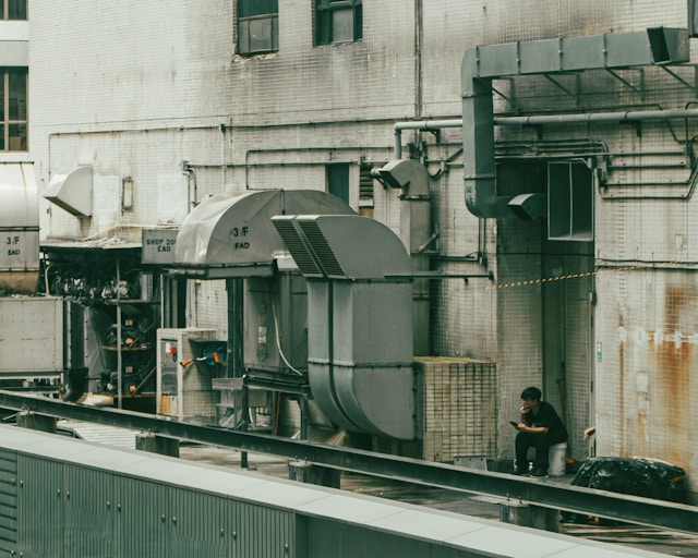 A person sits amidst industrial machinery outdoors